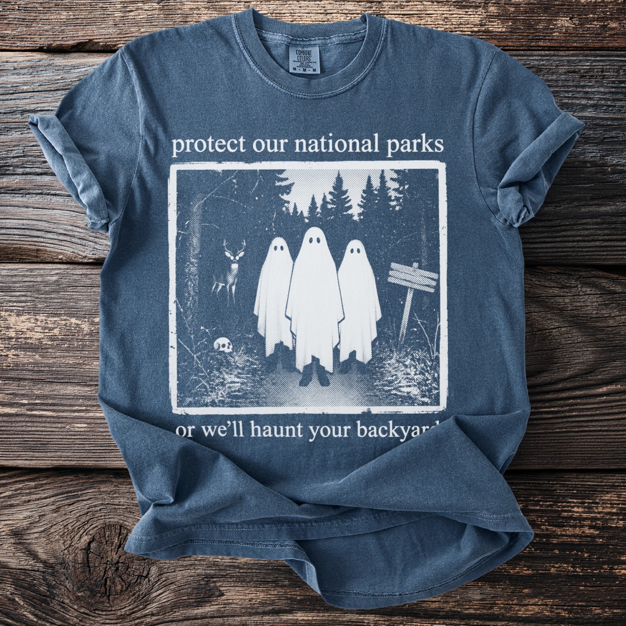 Blue t-shirt with ghosts, deer, skull, and trees. Text reads "protect our national parks or we'll haunt your backyard."