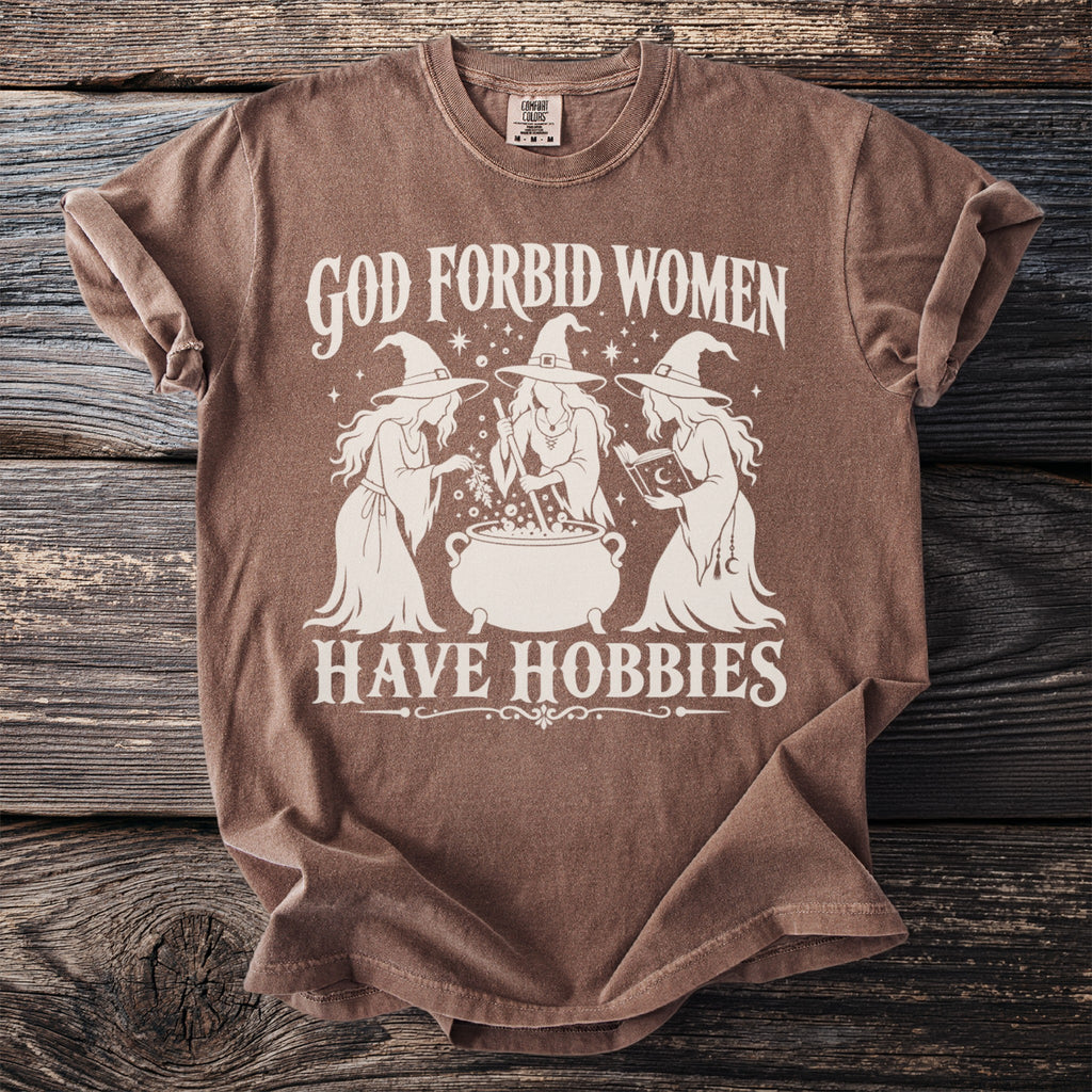 Brown t-shirt with white graphic text "God Forbid Women Have Hobbies" and three witches.