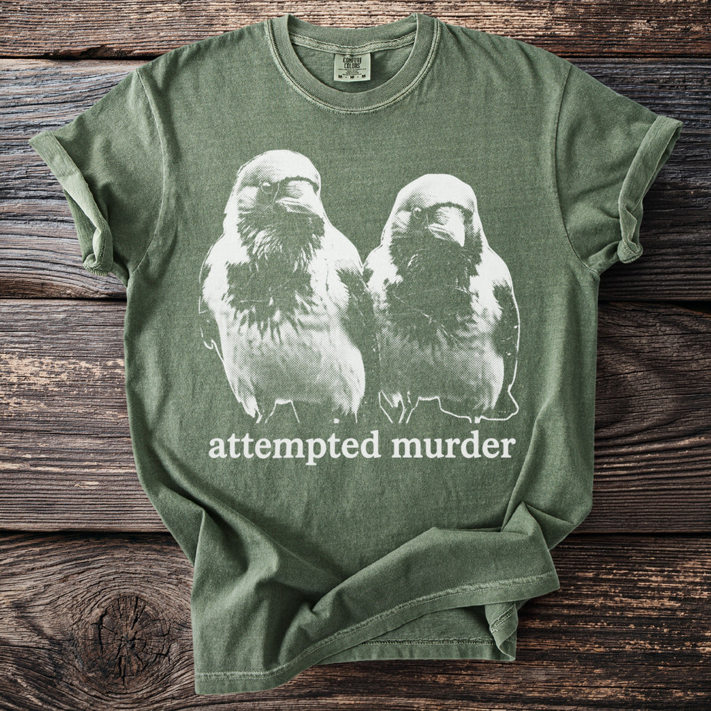 Green t-shirt with a graphic of two crows and the text "attempted murder".