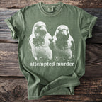 Green t-shirt with a graphic of two crows and the text "attempted murder".