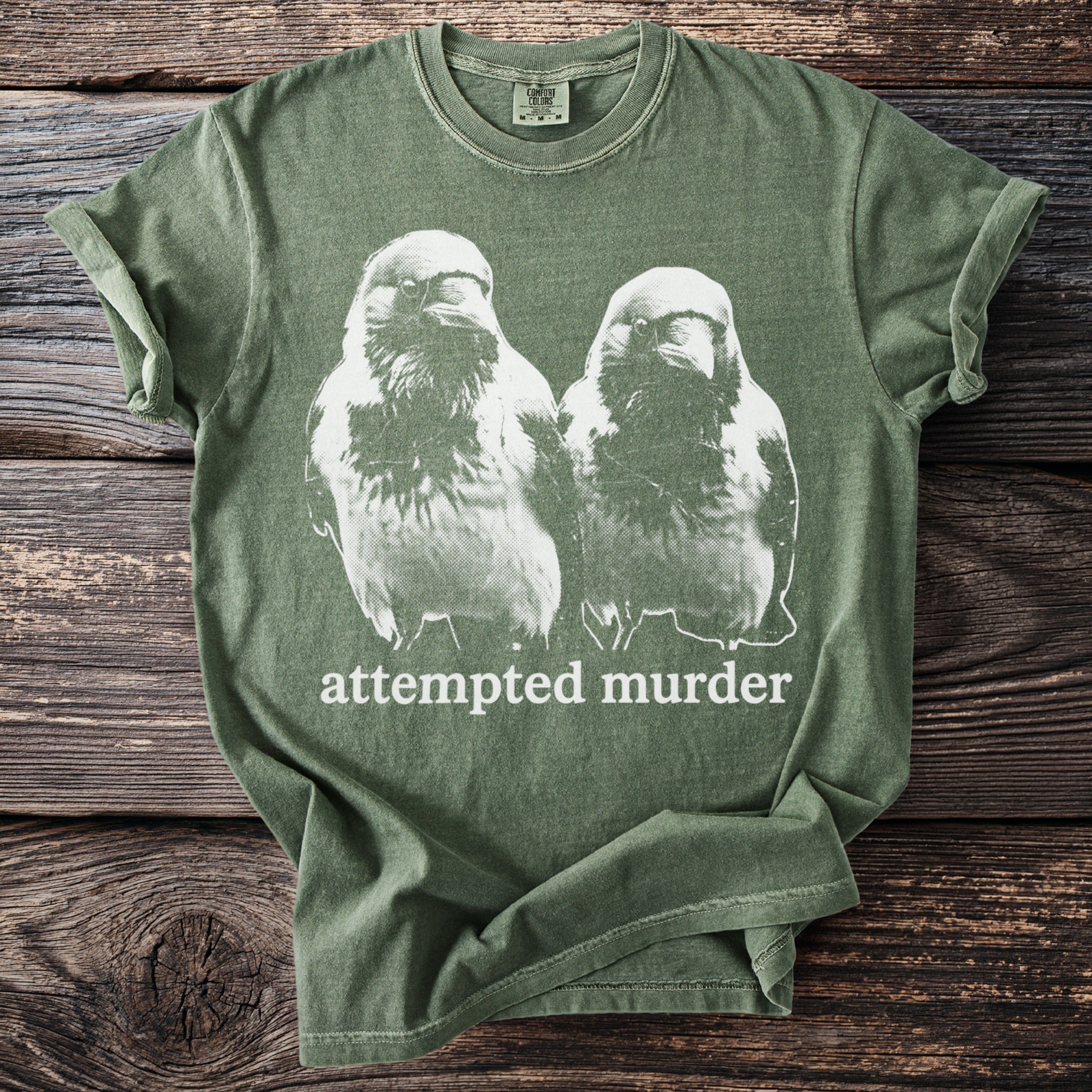 Green t-shirt with a graphic of two crows and the text "attempted murder".