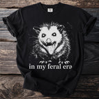 Black t-shirt with a white graphic of a screaming opossum and text "in my feral era".