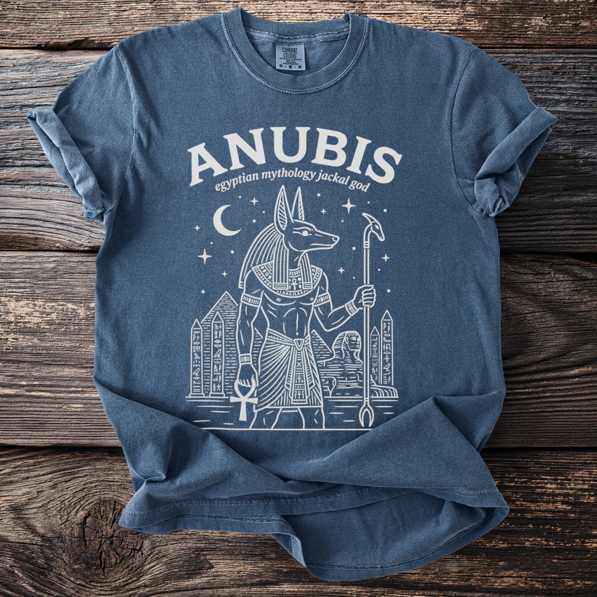Blue T-shirt with Anubis, Egyptian mythology jackal god, and pyramids graphic.
