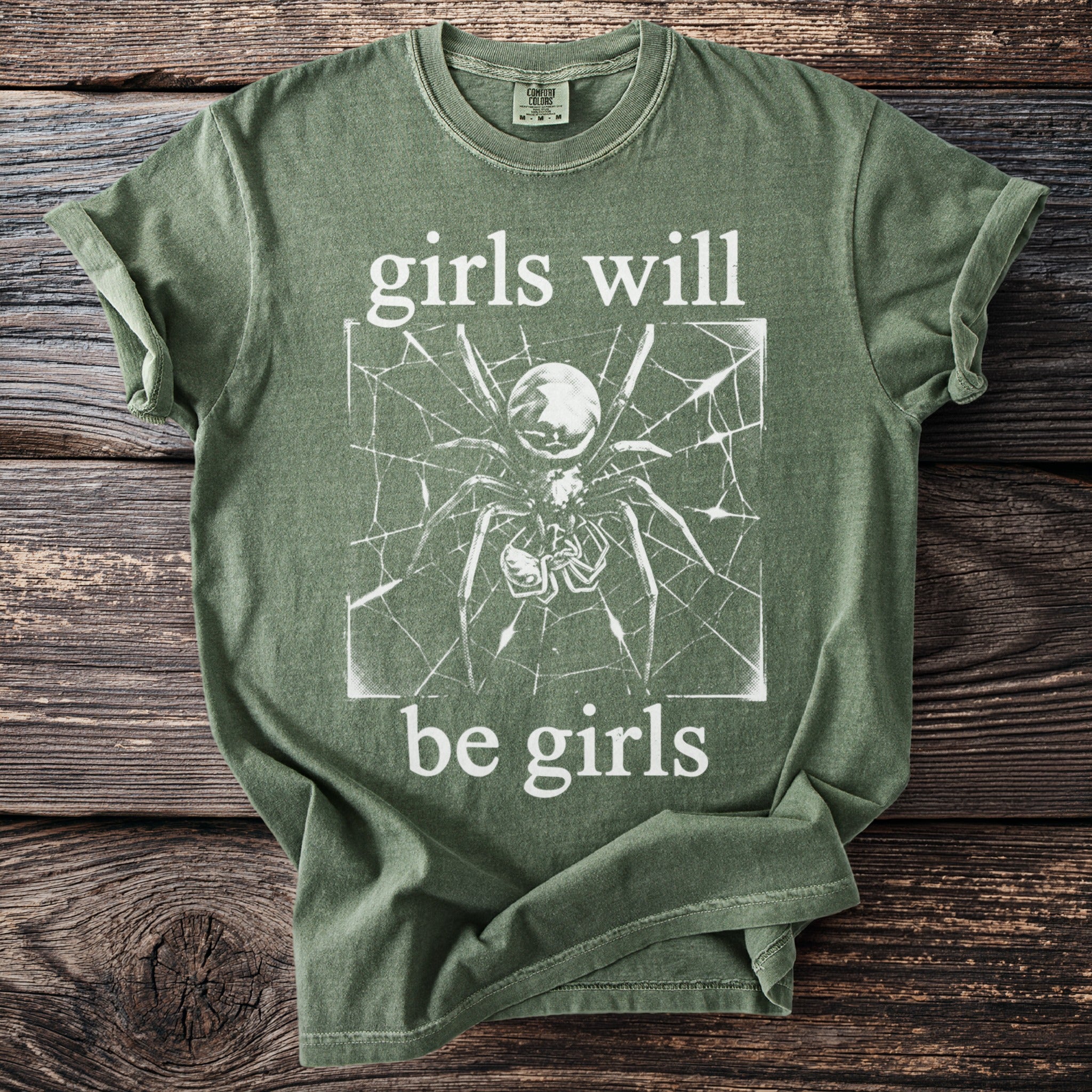 Green t-shirt with spider on web graphic and "girls will be girls" text.