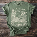 Green t-shirt with cream print of cat on spellbook, candles, and mushrooms.