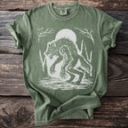 Green t-shirt with white werewolf and full moon graphic on wooded background.