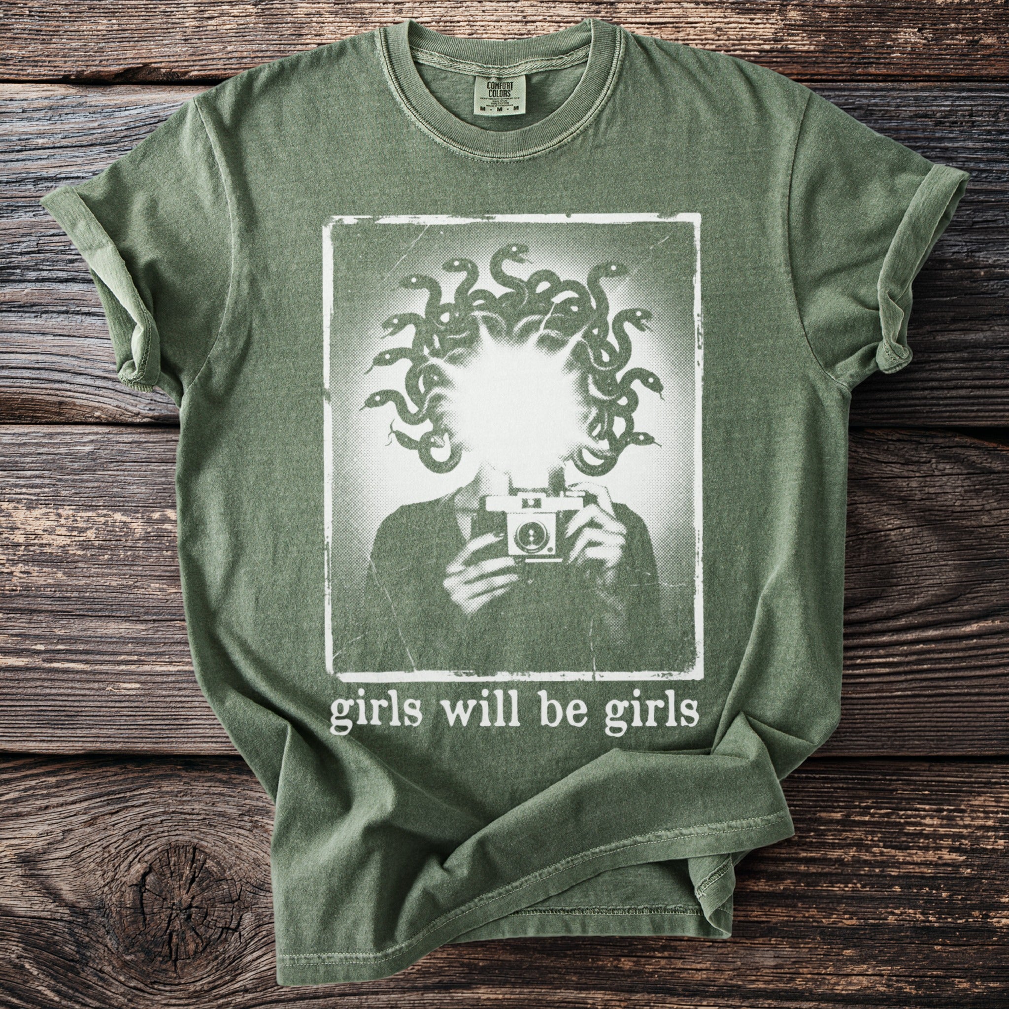 Green t-shirt with Medusa silhouette holding a camera, text "girls will be girls".
