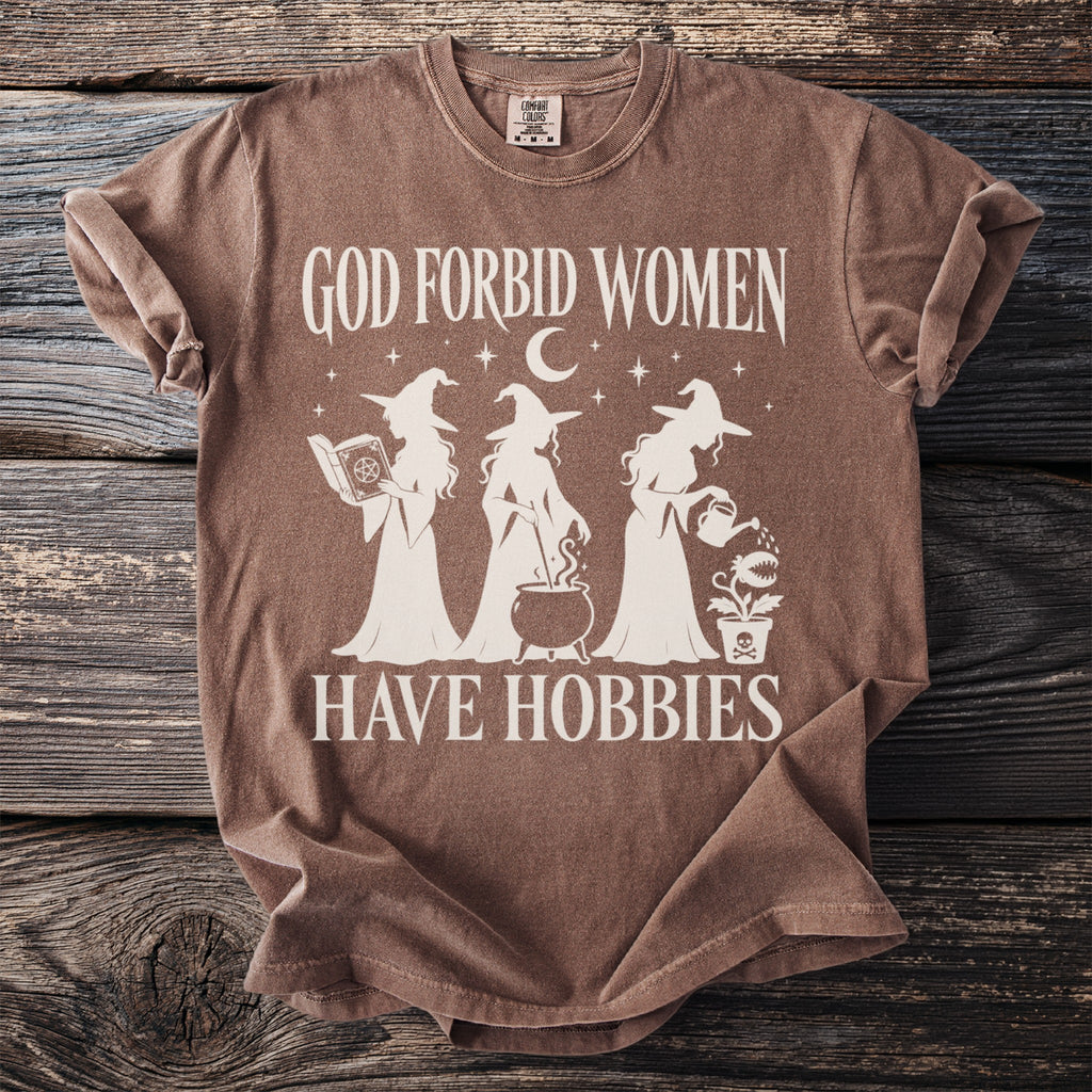 Brown t-shirt with white text "God Forbid Women Have Hobbies" and witch graphics.