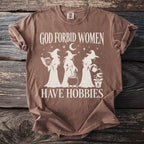 Brown t-shirt with white text "God Forbid Women Have Hobbies" and witch graphics.