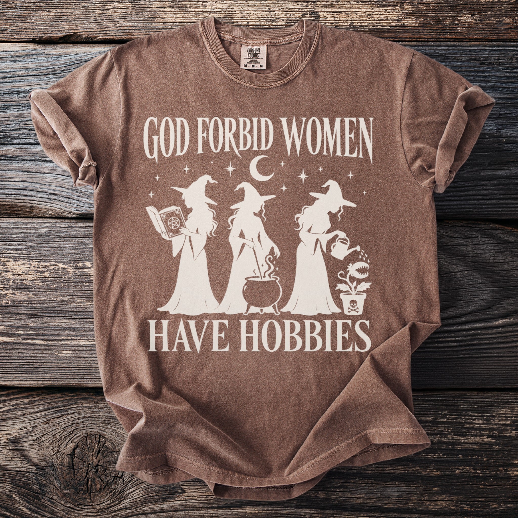 Brown t-shirt with white text "God Forbid Women Have Hobbies" and witch graphics.