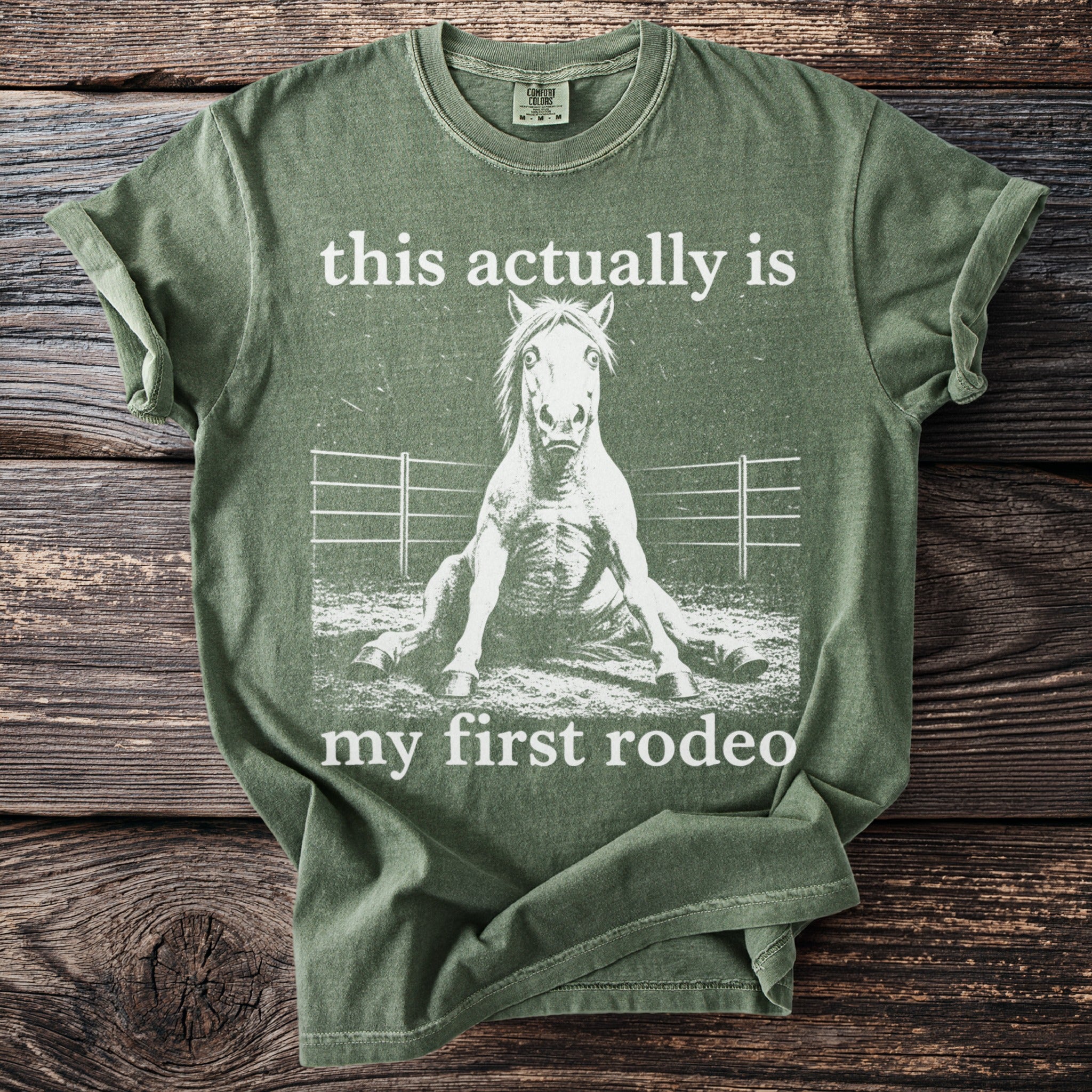 Green t-shirt with white graphic of a horse sitting down and text "this actually is my first rodeo".