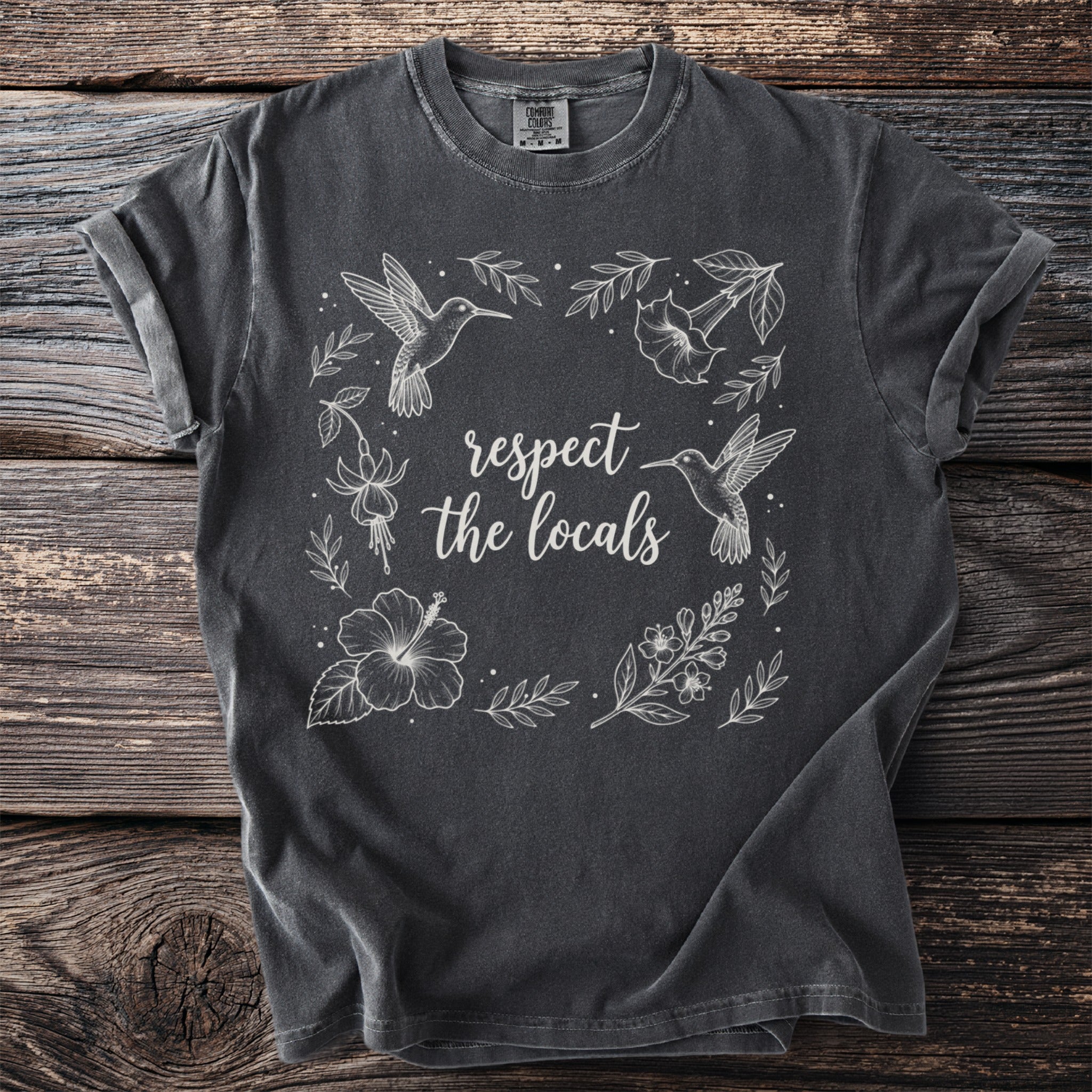 Dark grey t-shirt with white line art of hummingbirds, flowers, and text that reads "respect the locals."