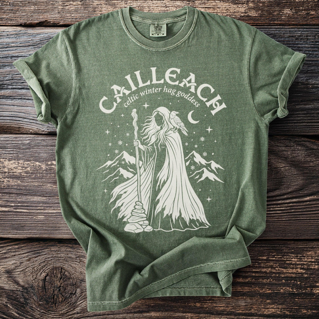 Green t-shirt with a cream graphic depicting the "Cailleach, Celtic winter hag goddess".