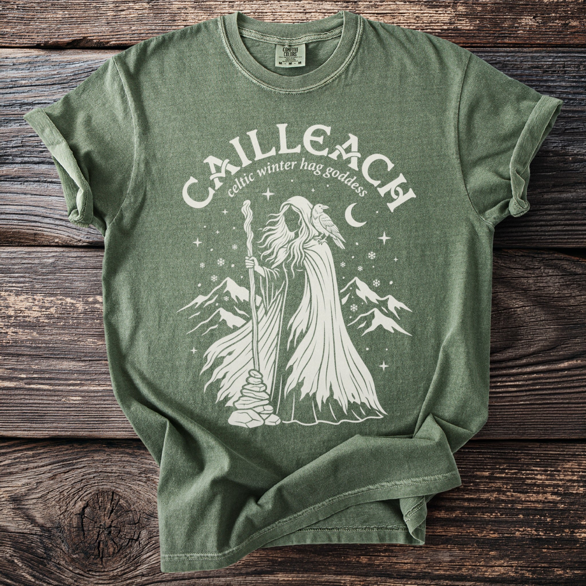 Green t-shirt with a cream graphic depicting the "Cailleach, Celtic winter hag goddess".