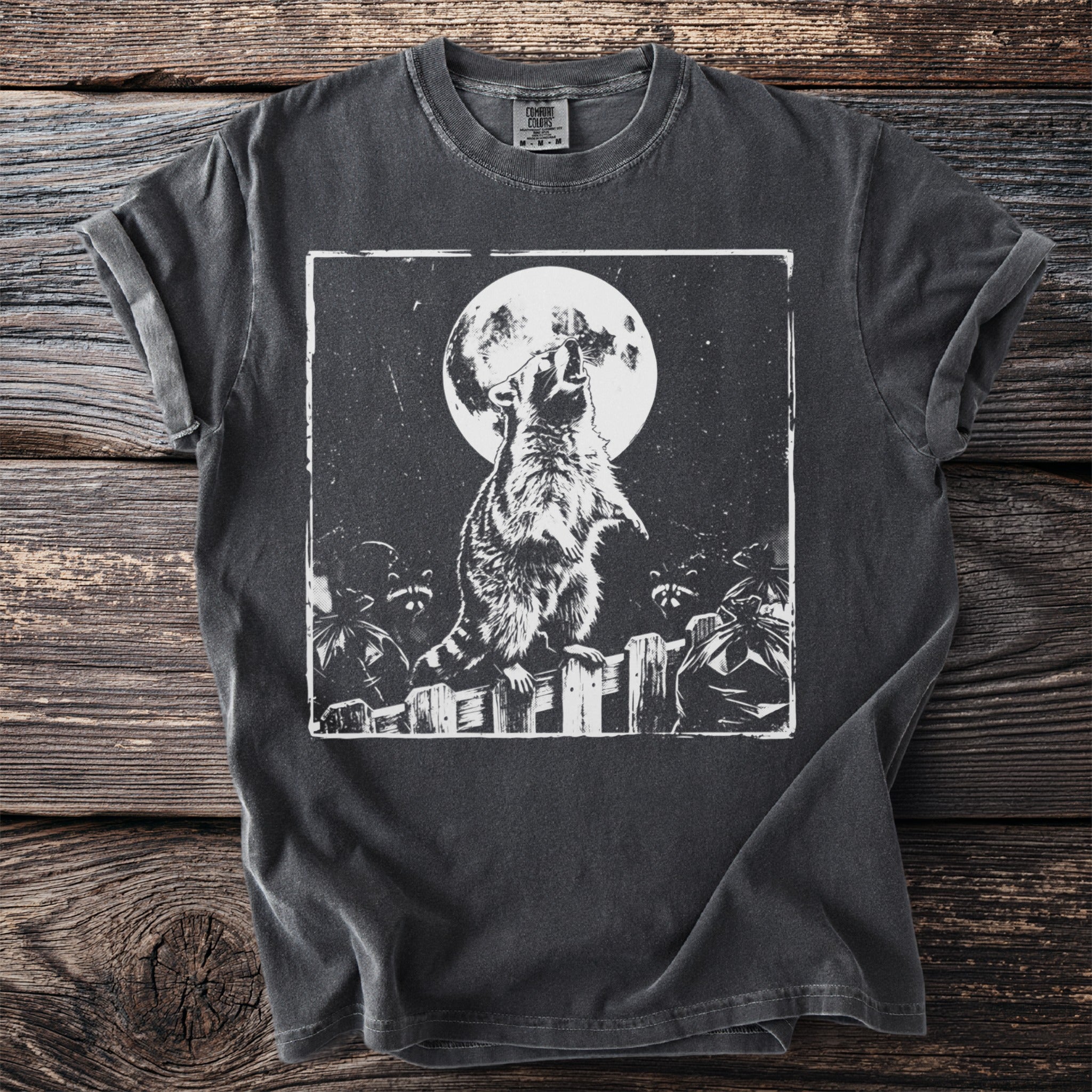 Dark t-shirt with a black and white graphic of a raccoon howling at the full moon.
