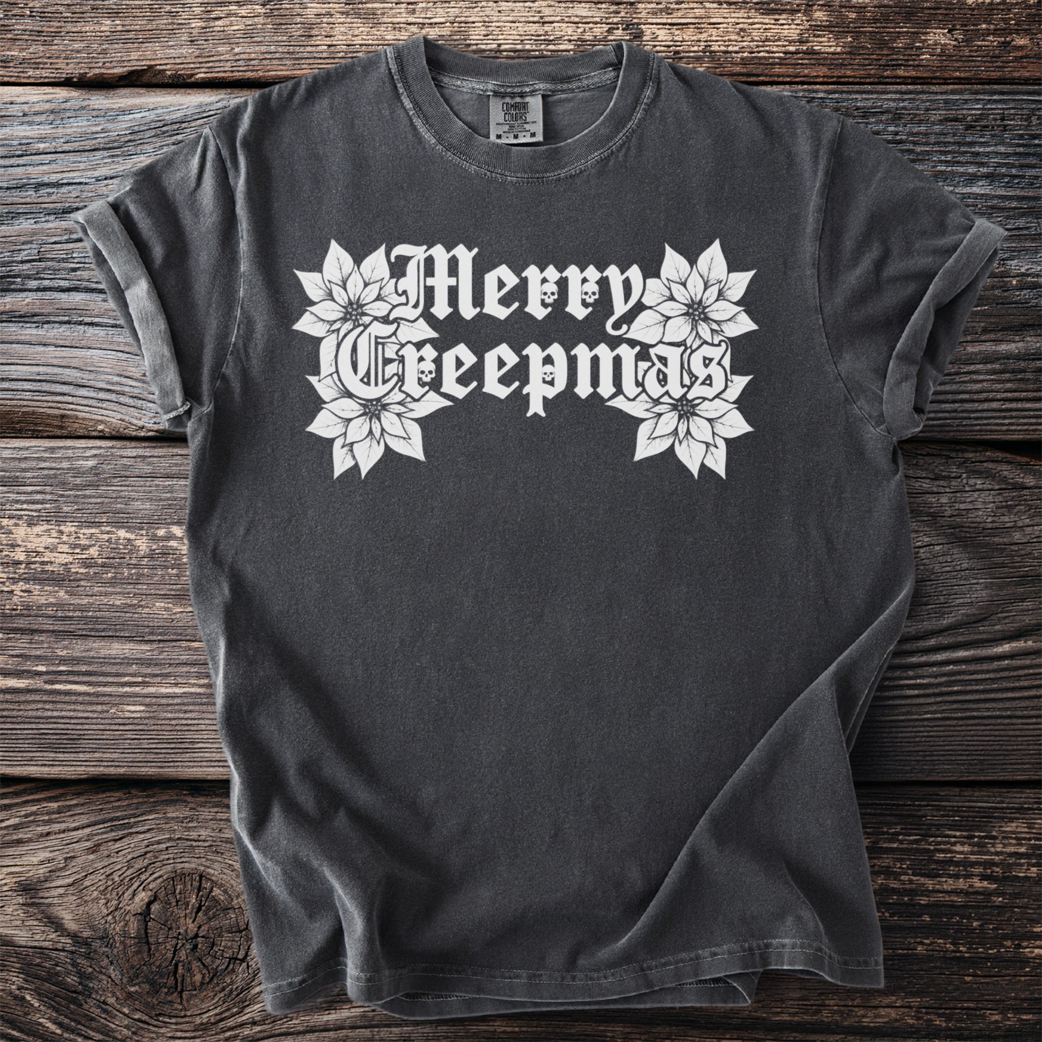 Dark grey t-shirt with white gothic text "Merry Creepmas" and poinsettias.