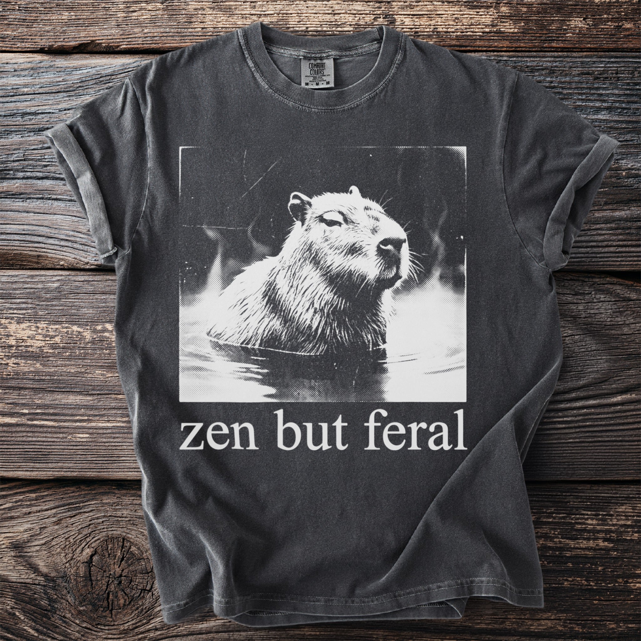 T-shirt with black and white capybara in water graphic and "zen but feral" text.