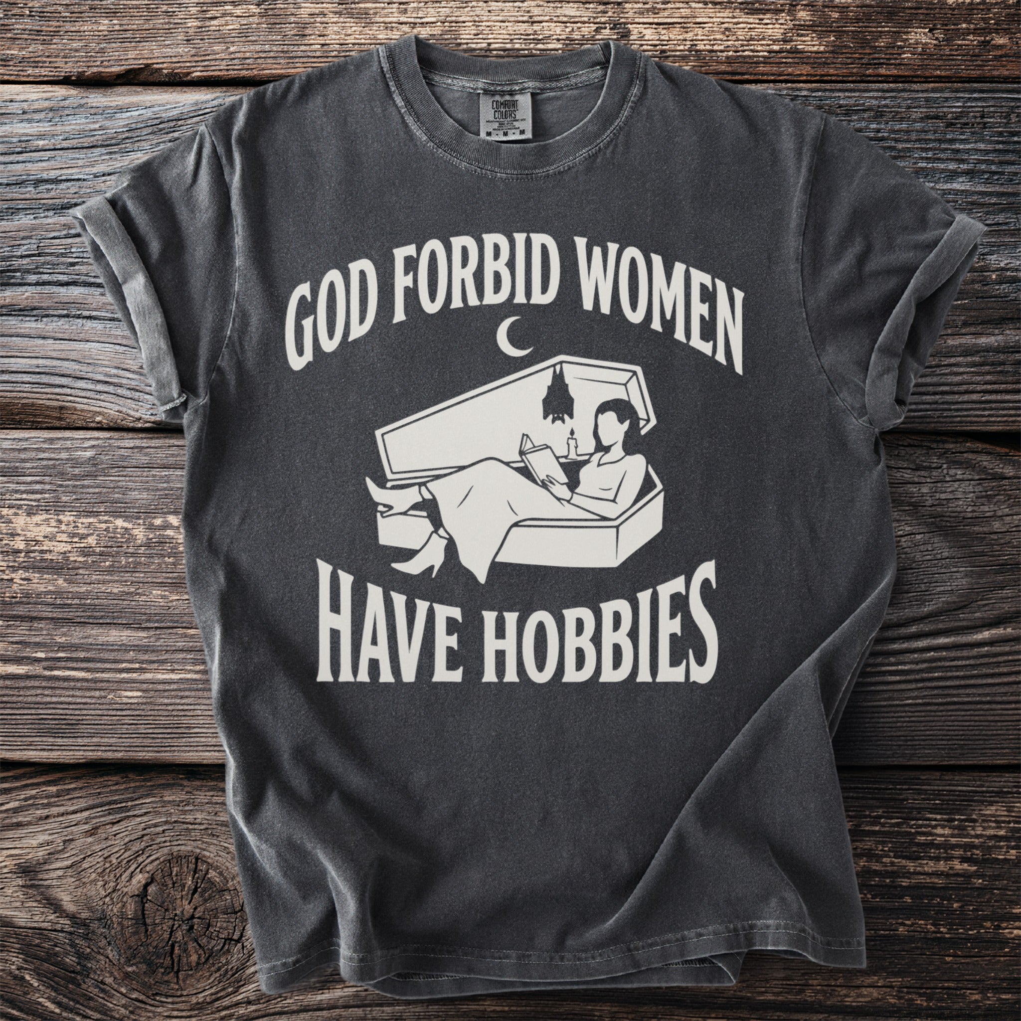 Dark grey t-shirt with white text "GOD FORBID WOMEN" and a coffin graphic with a person reading.