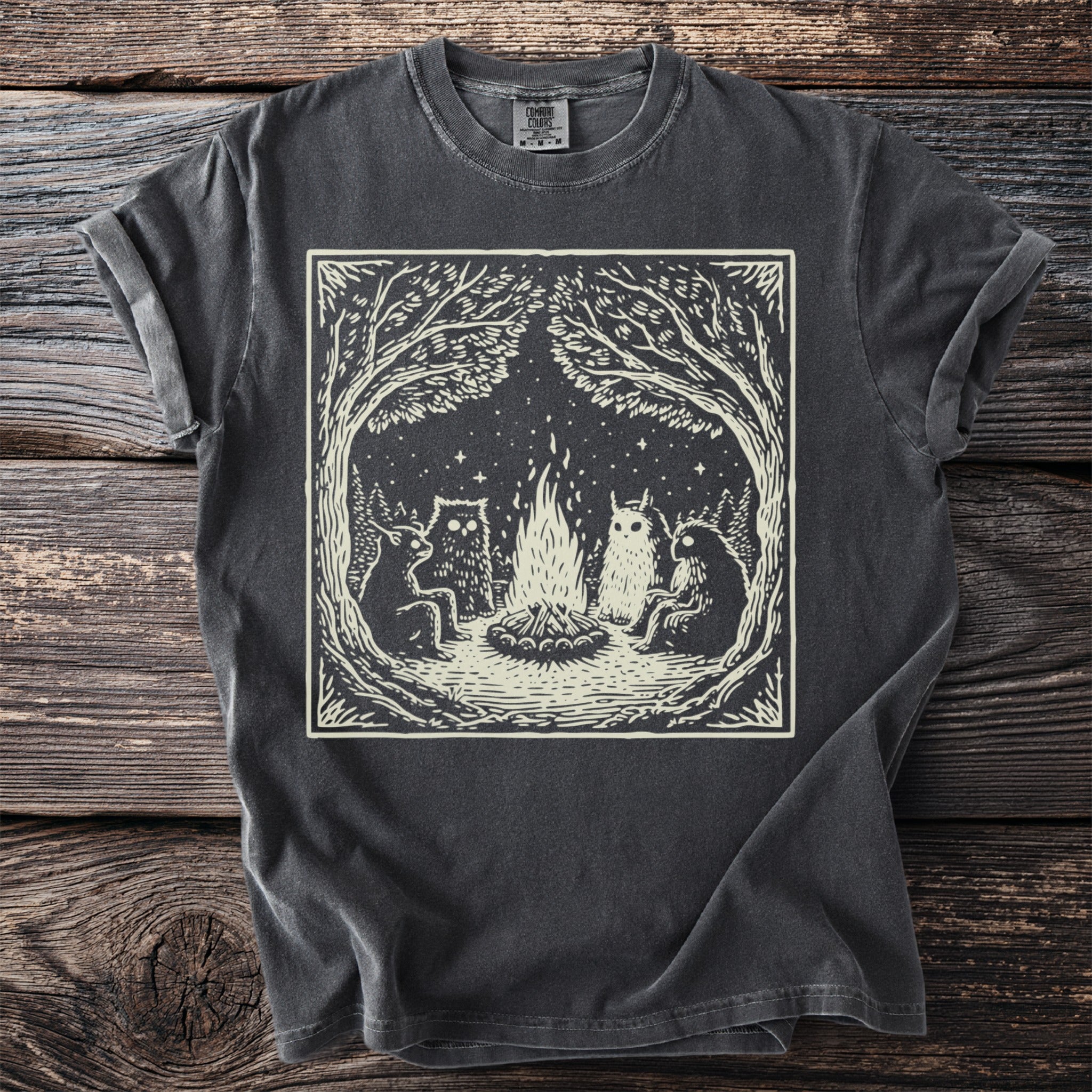 Dark grey t-shirt with a cream linocut design of woodland creatures around a campfire.
