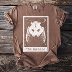 Brown t-shirt with a tarot card design featuring a white opossum, moon, and stars.