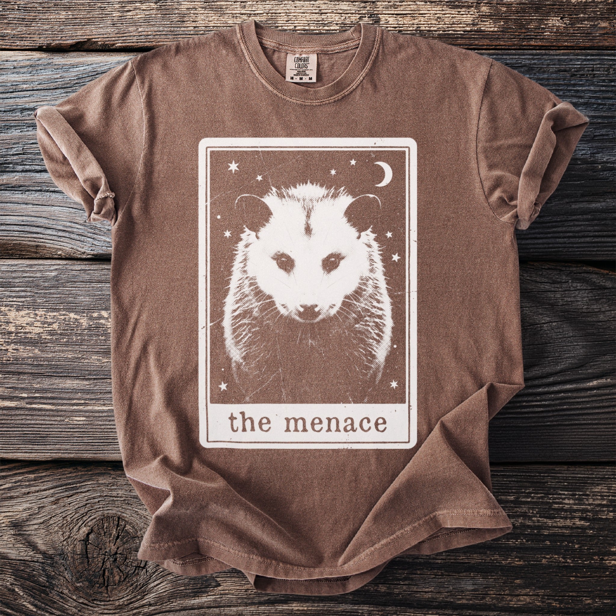 Brown t-shirt with a tarot card design featuring a white opossum, moon, and stars.