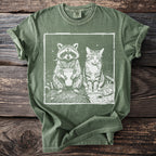 Green t-shirt featuring white graphic of raccoon with drink and cat smoking