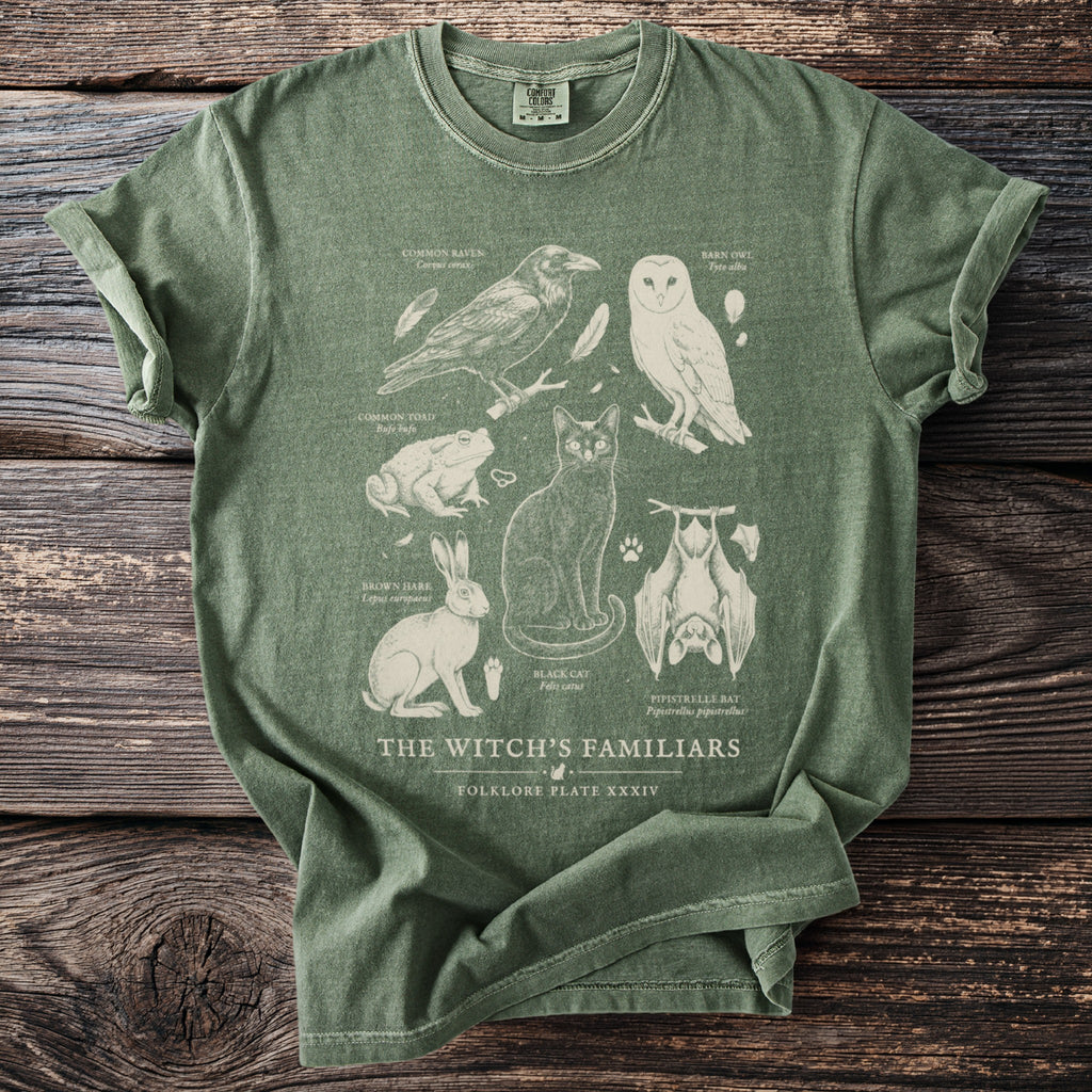Green t-shirt with illustrations of a raven, barn owl, toad, rabbit, cat, and bat titled "The Witch's Familiars".