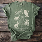 Green t-shirt with illustrations of a raven, barn owl, toad, rabbit, cat, and bat titled "The Witch's Familiars".