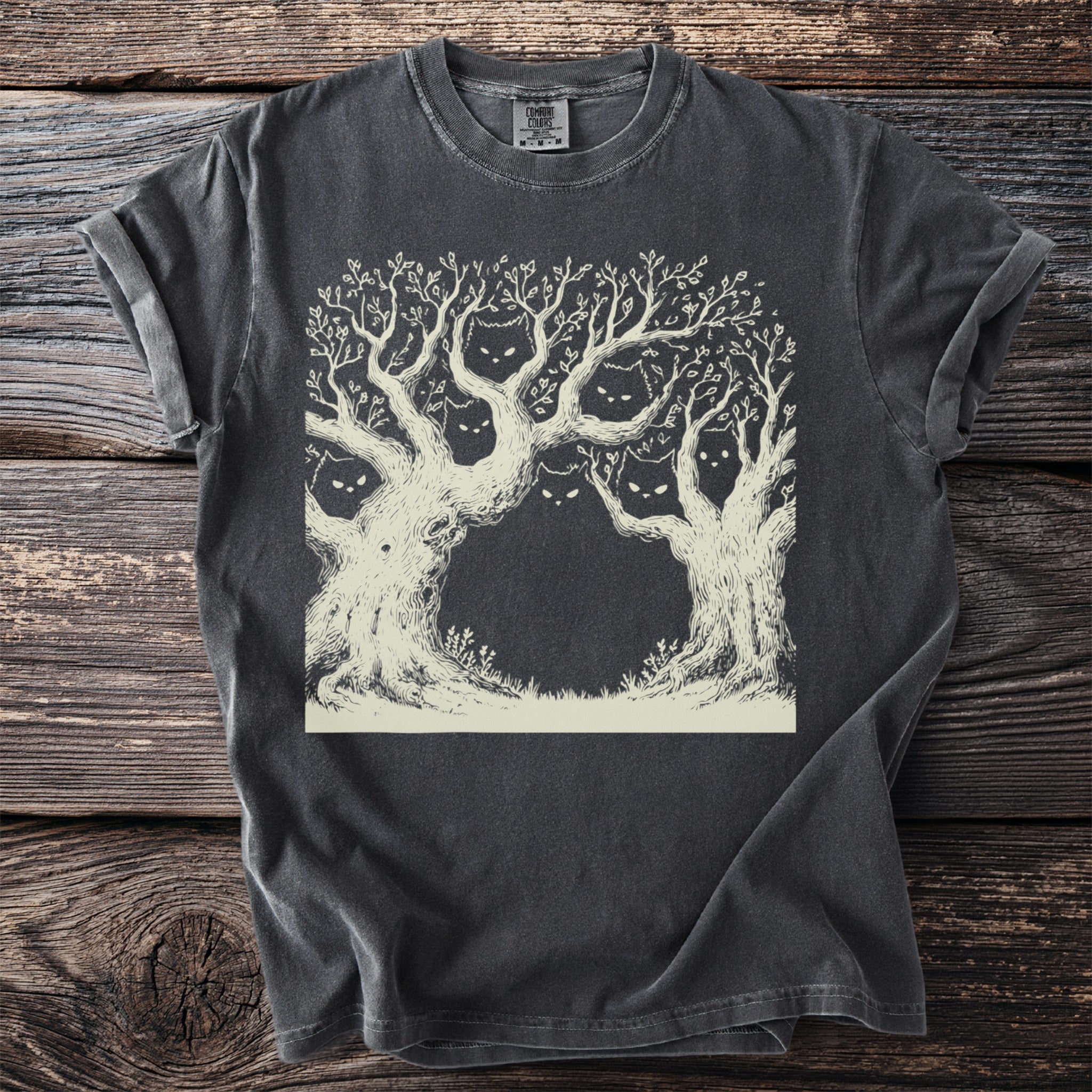 T-shirt with a faded black distressed look featuring a light brown line drawing of trees with hidden cat faces.