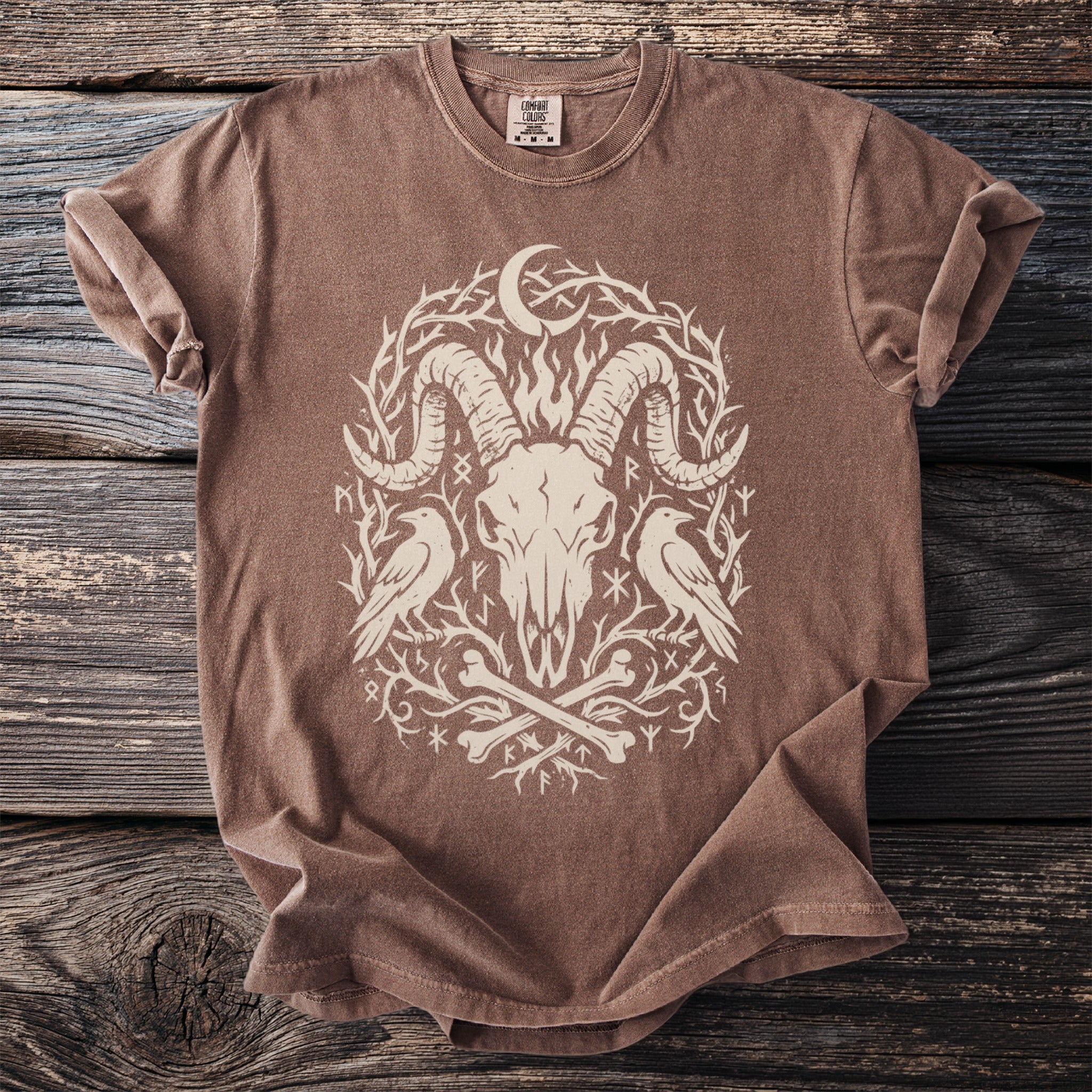Brown Comfort Colors t-shirt with a cream ram skull, moon, crows, and runes design.