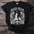 Black t-shirt with a white witch, cat, moon, and floral border design.