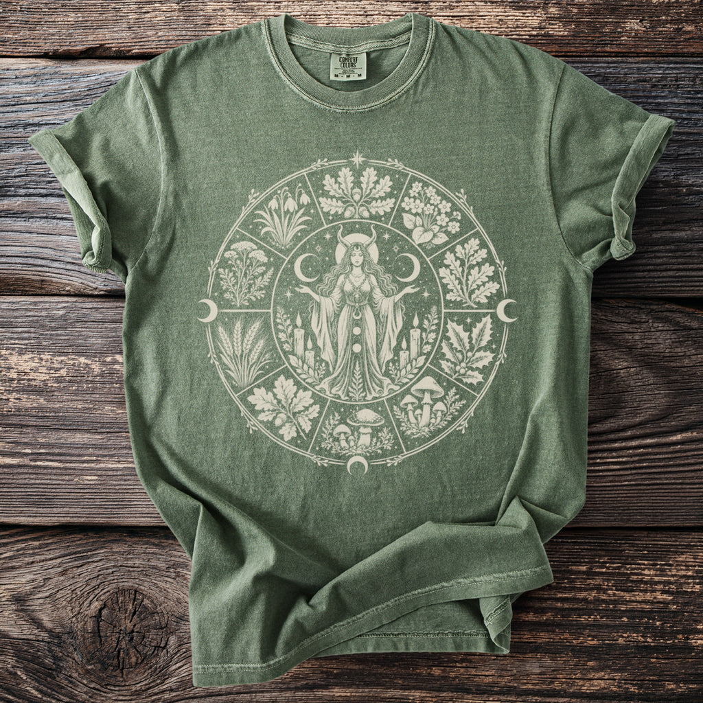 Green t-shirt with a white circular design featuring a goddess, celestial bodies, and botanical elements.