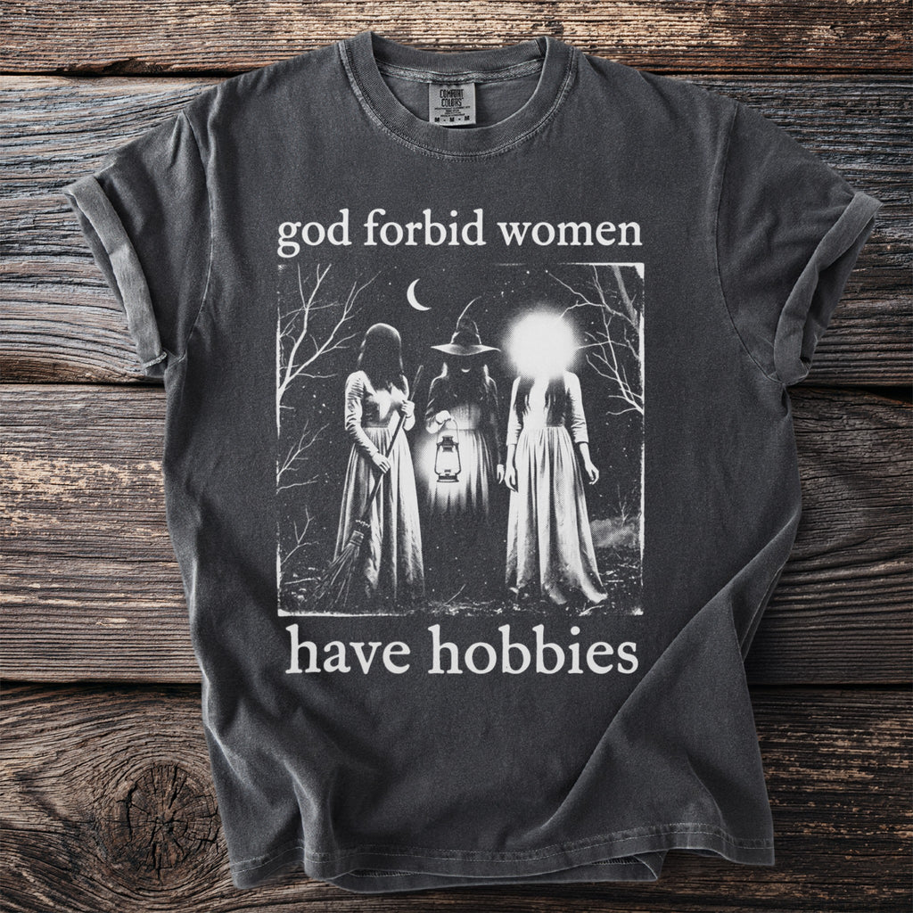 Dark t-shirt with "god forbid women have hobbies" and a night scene graphic.
