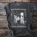 Dark t-shirt with "god forbid women have hobbies" and a night scene graphic.