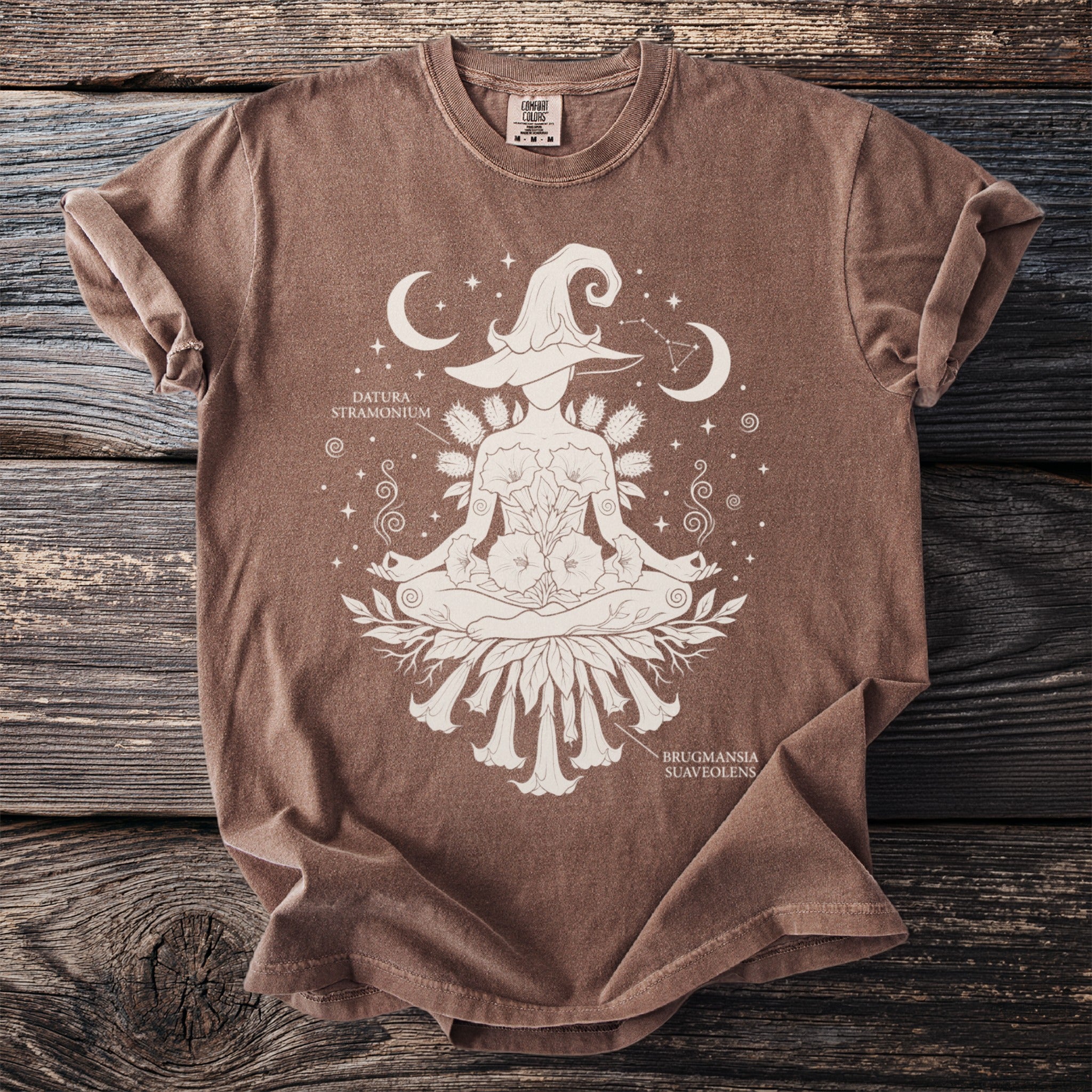 Brown t-shirt with white graphic of a meditating witch hat figure with datura and brugmansia.