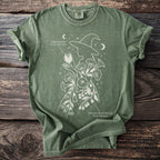 Green t-shirt with white line art of a witch silhouette surrounded by Jimsonweed and Deadly Nightshade plants.