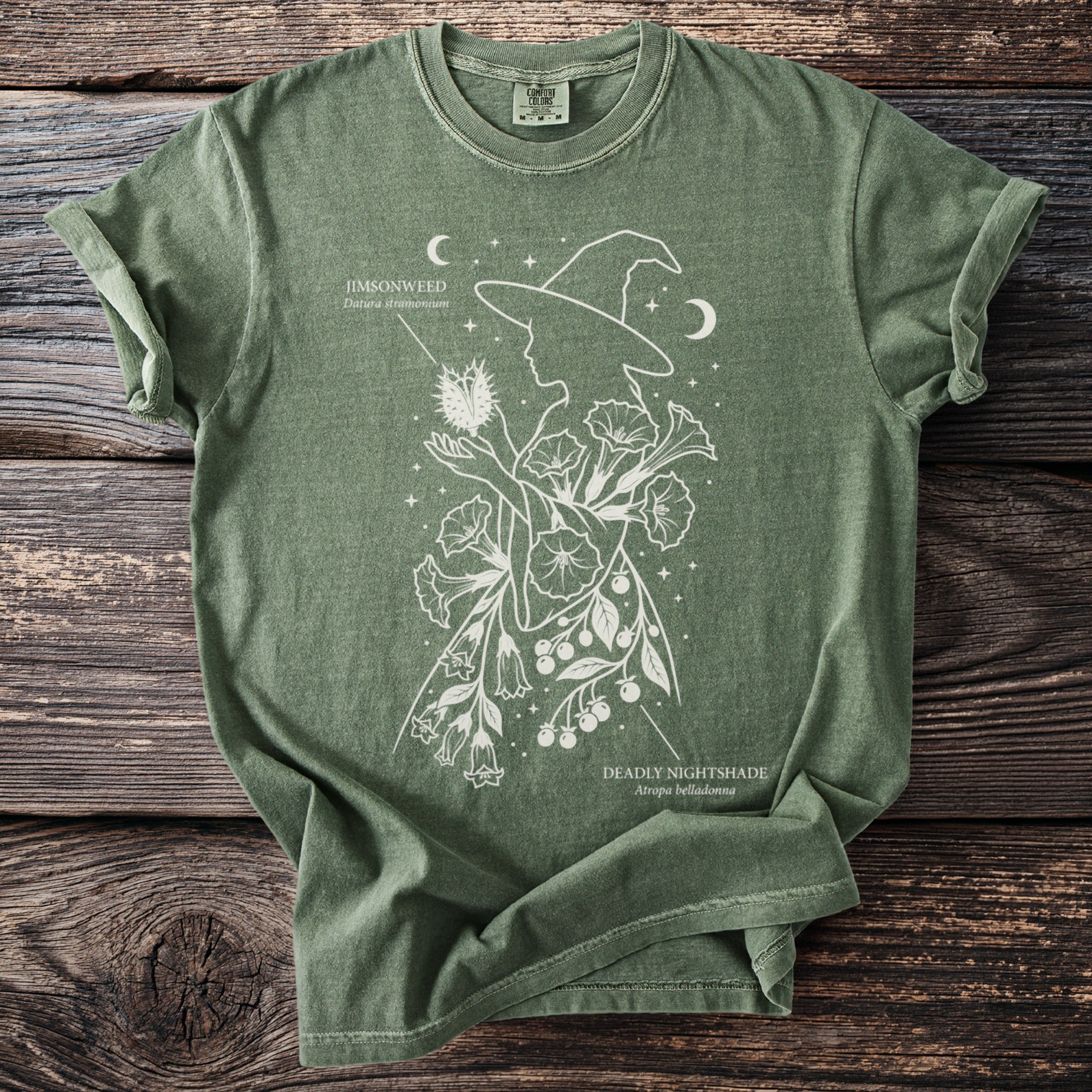 Green t-shirt with white line art of a witch silhouette surrounded by Jimsonweed and Deadly Nightshade plants.