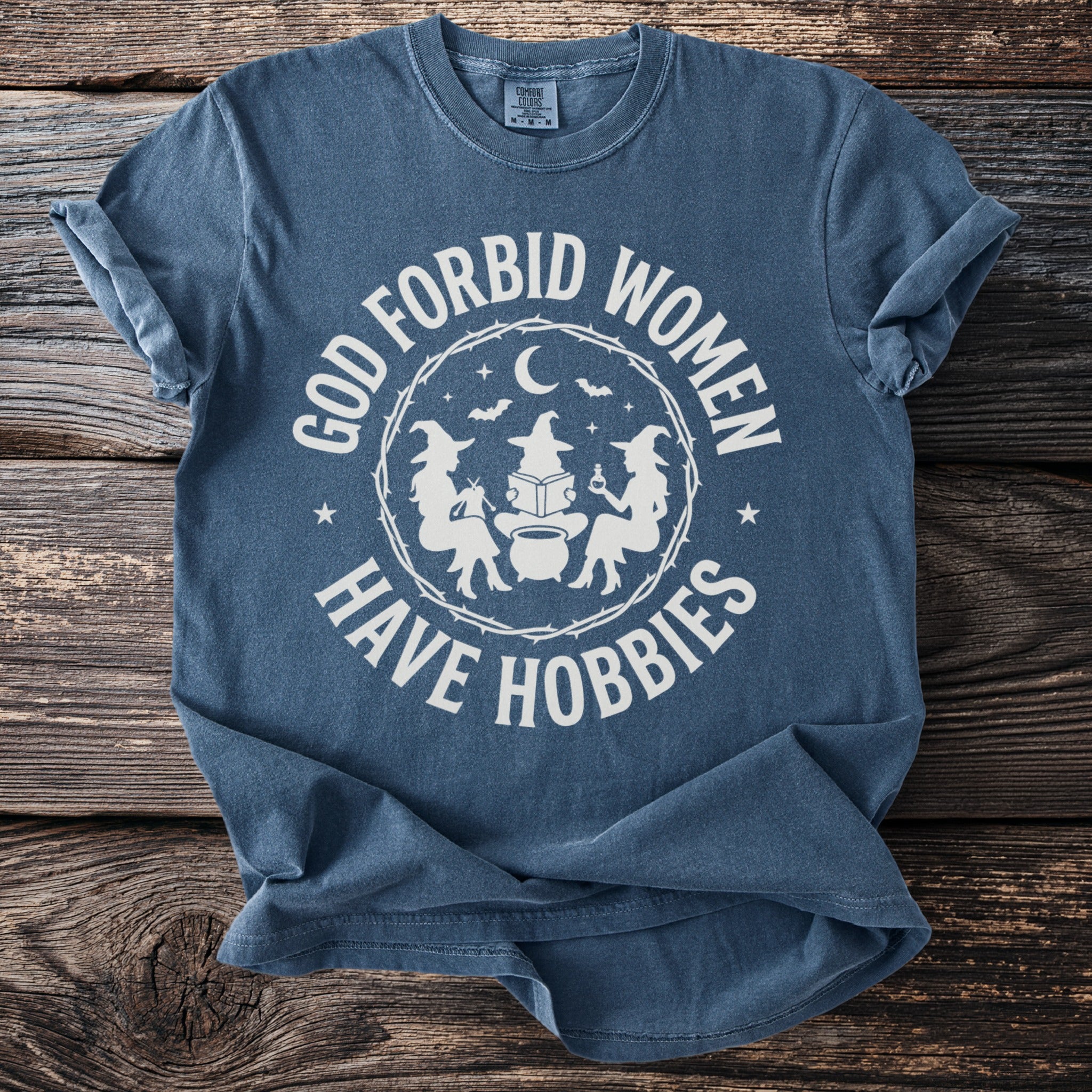 Blue t-shirt with "God Forbid Women Have Hobbies" and witchy graphics.