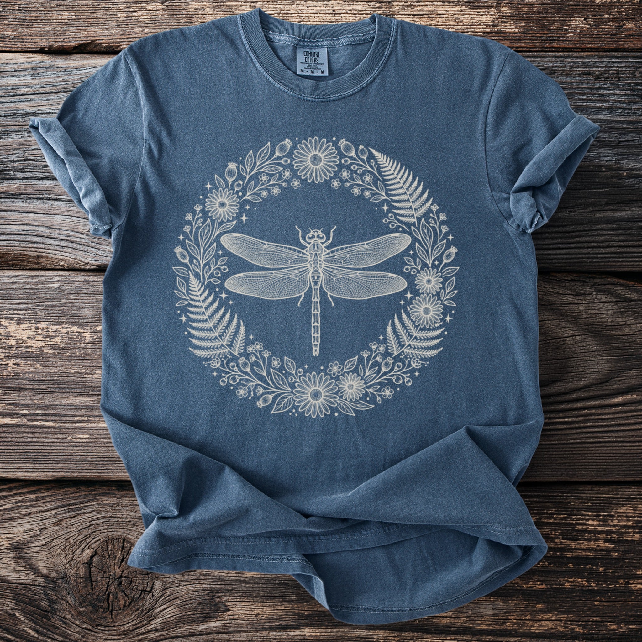 Blue t-shirt with a cream outline of a dragonfly in a floral wreath.