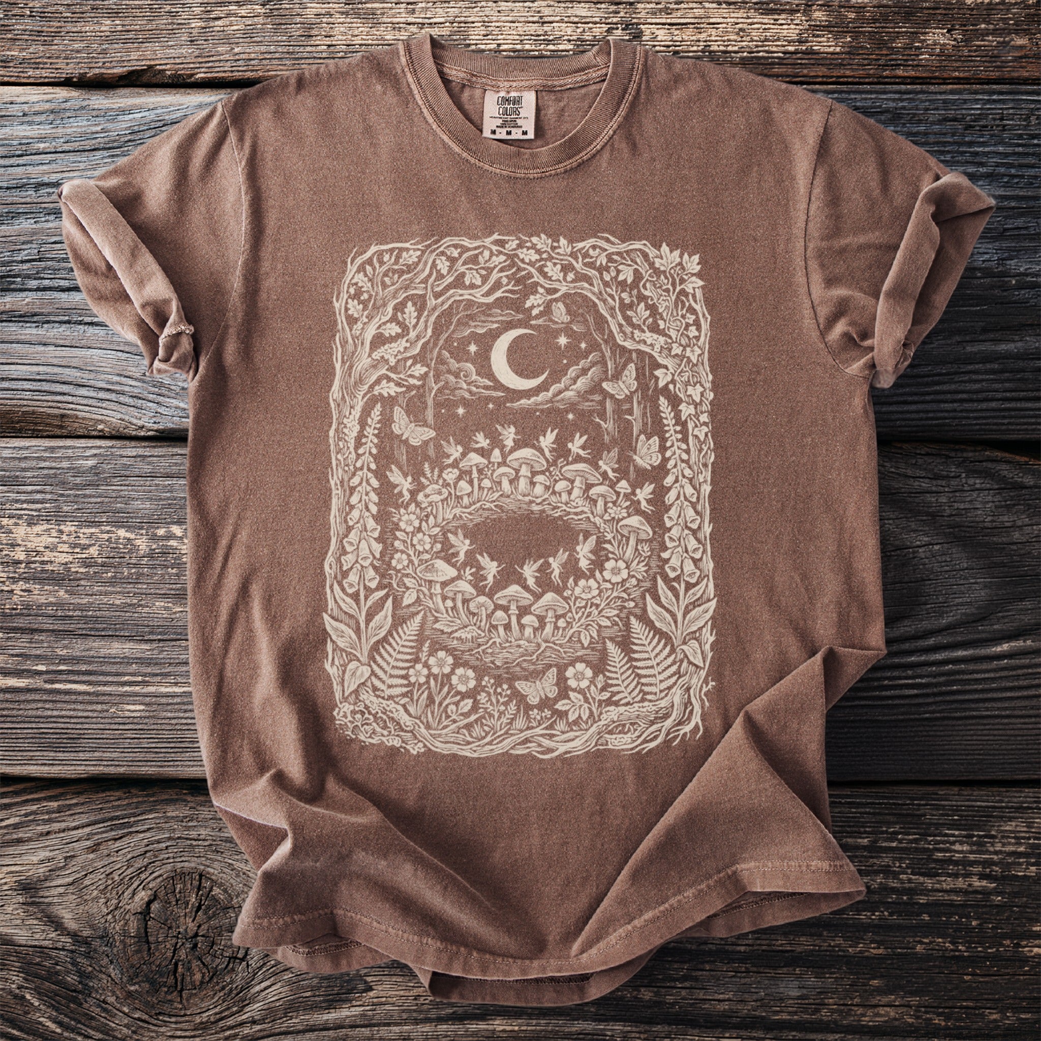Brown t-shirt with a cream intricate forest, moon, and fairy design.