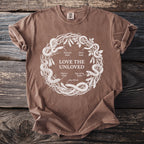 Brown t-shirt with white circular design of snakes and text "LOVE THE UNLOVED".