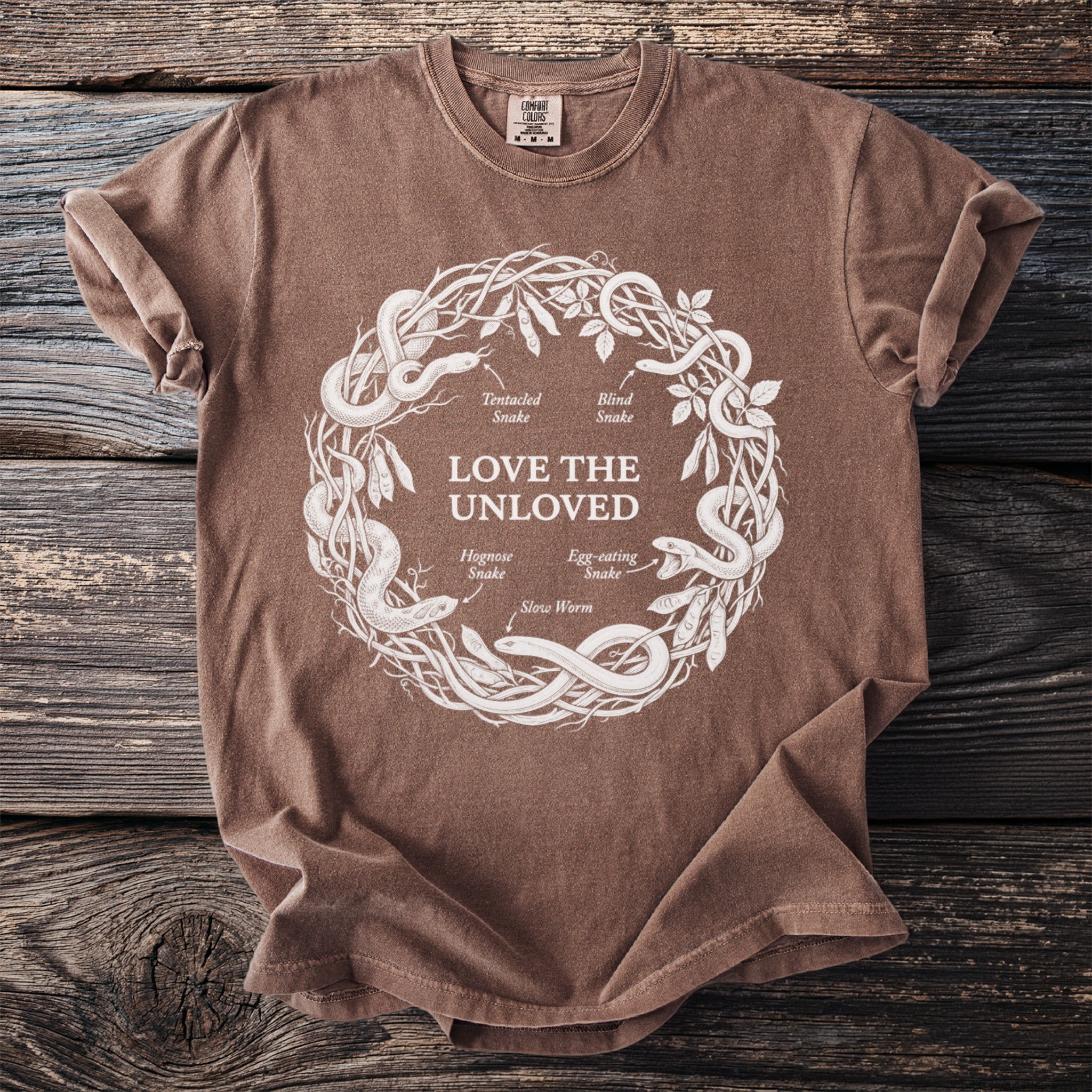 Brown t-shirt with white circular design of snakes and text "LOVE THE UNLOVED".