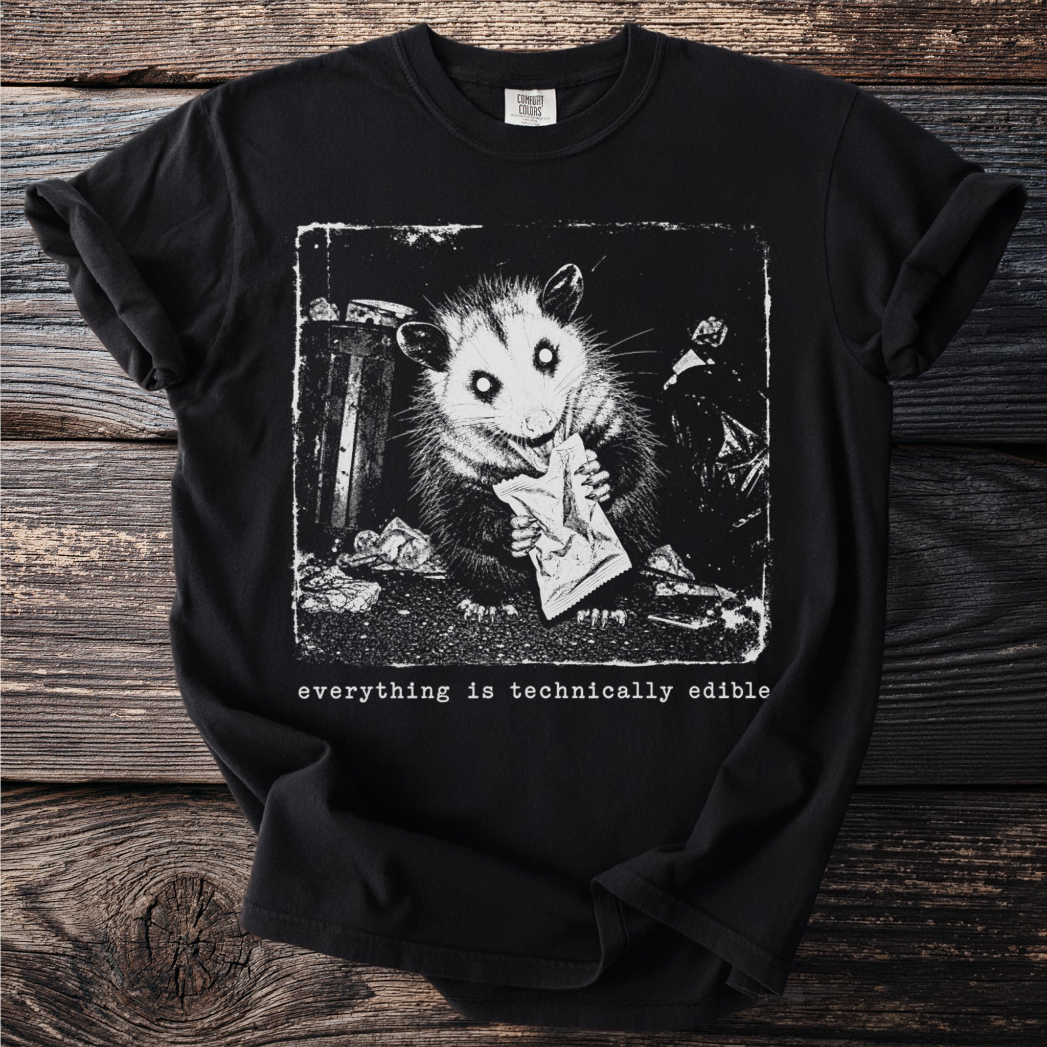 Black t-shirt with a distressed print of an opossum eating from a trash can, text reads "everything is technically edible".