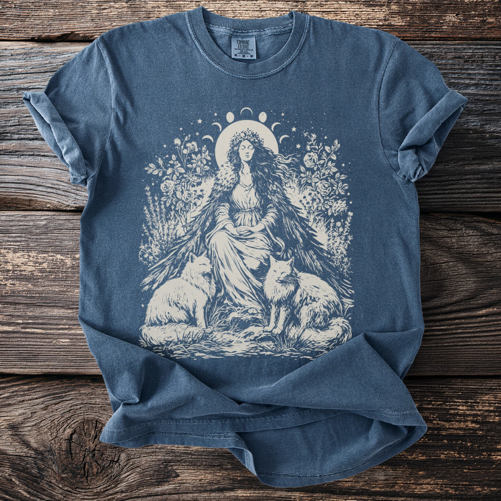 Blue t-shirt with illustration of crowned woman sitting between two foxes and floral elements.