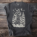 Pepper gray t-shirt with a cream folk-cut print: Mothman wraps himself and a small fir tree in Christmas lights, wings spread.