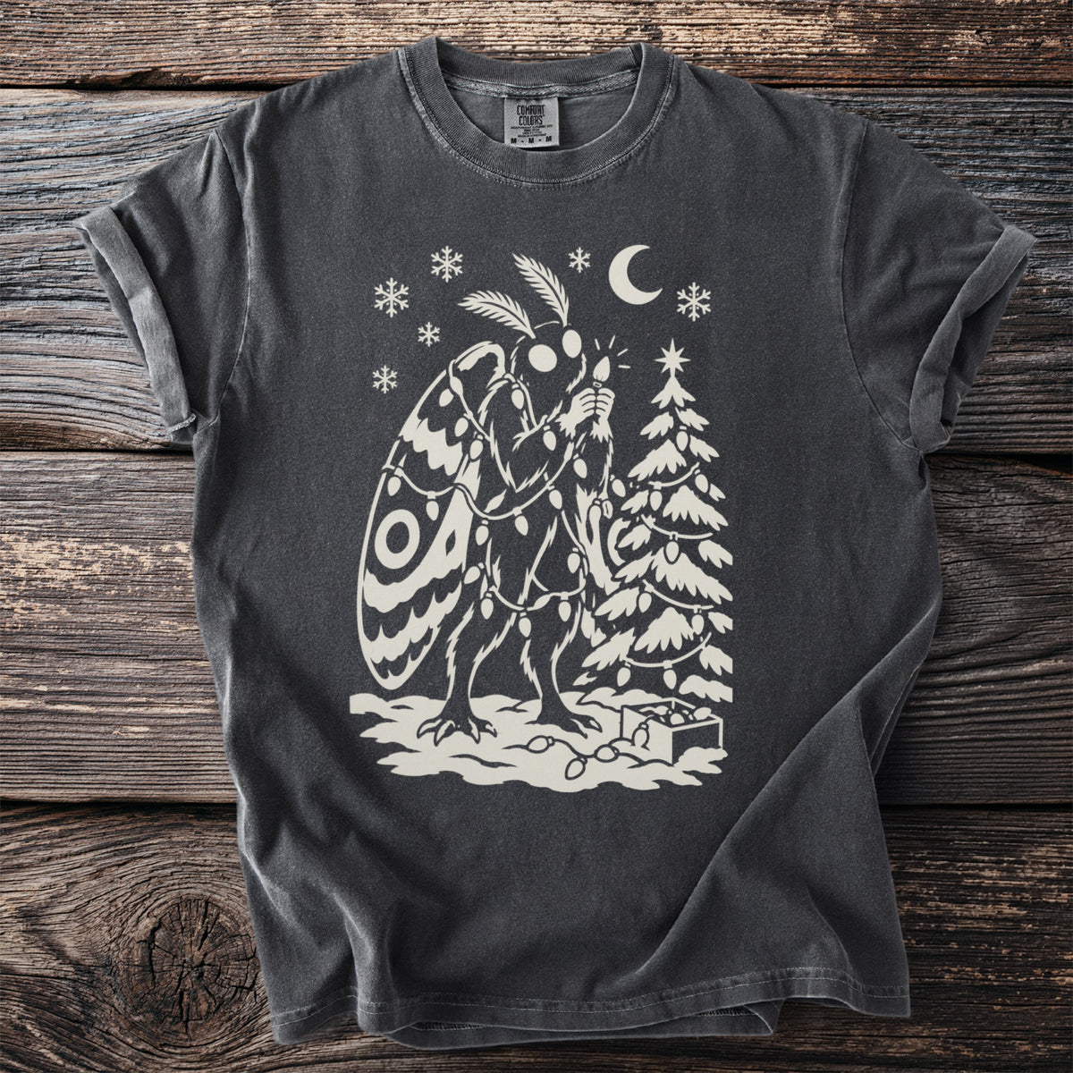 Pepper gray t-shirt with a cream folk-cut print: Mothman wraps himself and a small fir tree in Christmas lights, wings spread.