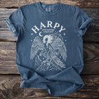 Blue t-shirt with white line art of a harpy, Greek mythology, winged spirit above mountains.