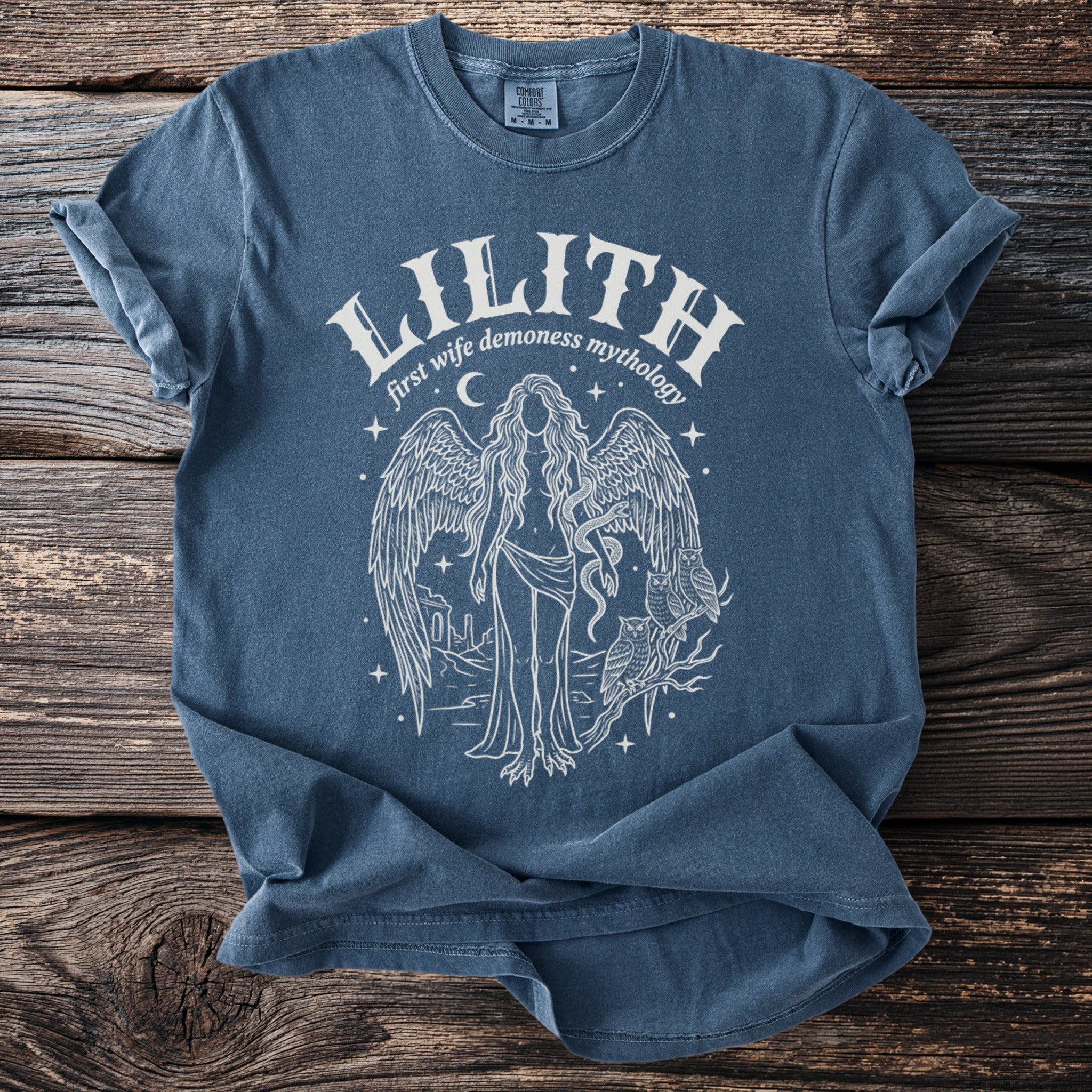 Blue t-shirt with "Lilith first wife demoness mythology" and an illustration of a winged figure.