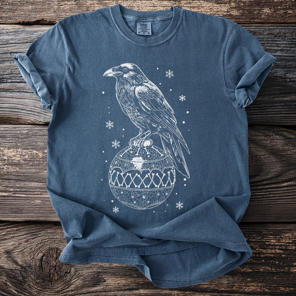 Blue t-shirt with white outline of raven perched on an ornate Christmas ornament.