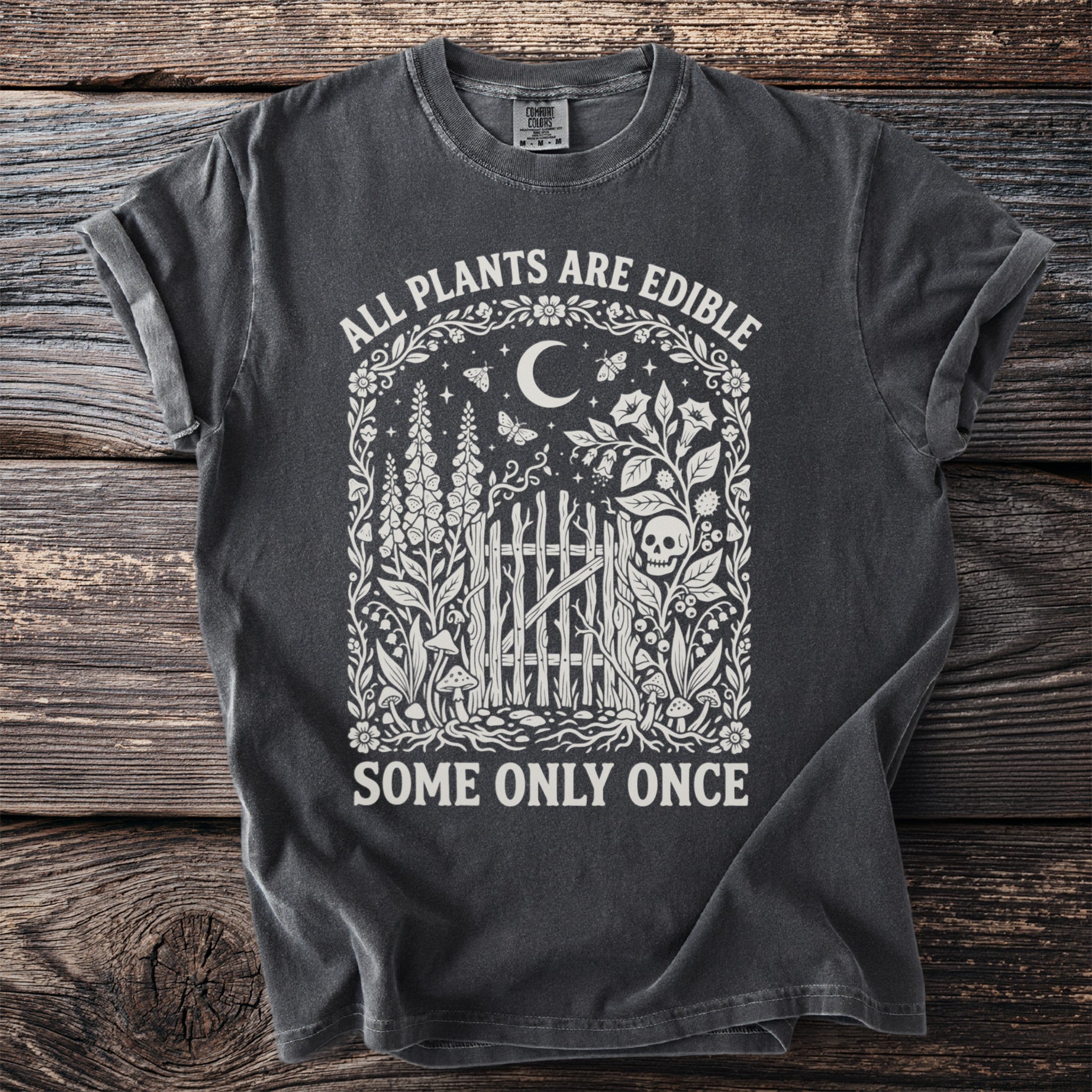 Dark t-shirt with Gothic design of plants, skull and text: "ALL PLANTS ARE EDIBLE, SOME ONLY ONCE."